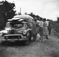 Ron Church – Sunset Beach, Tourists (Women) Looking at Surfboards on Car, circa 1963